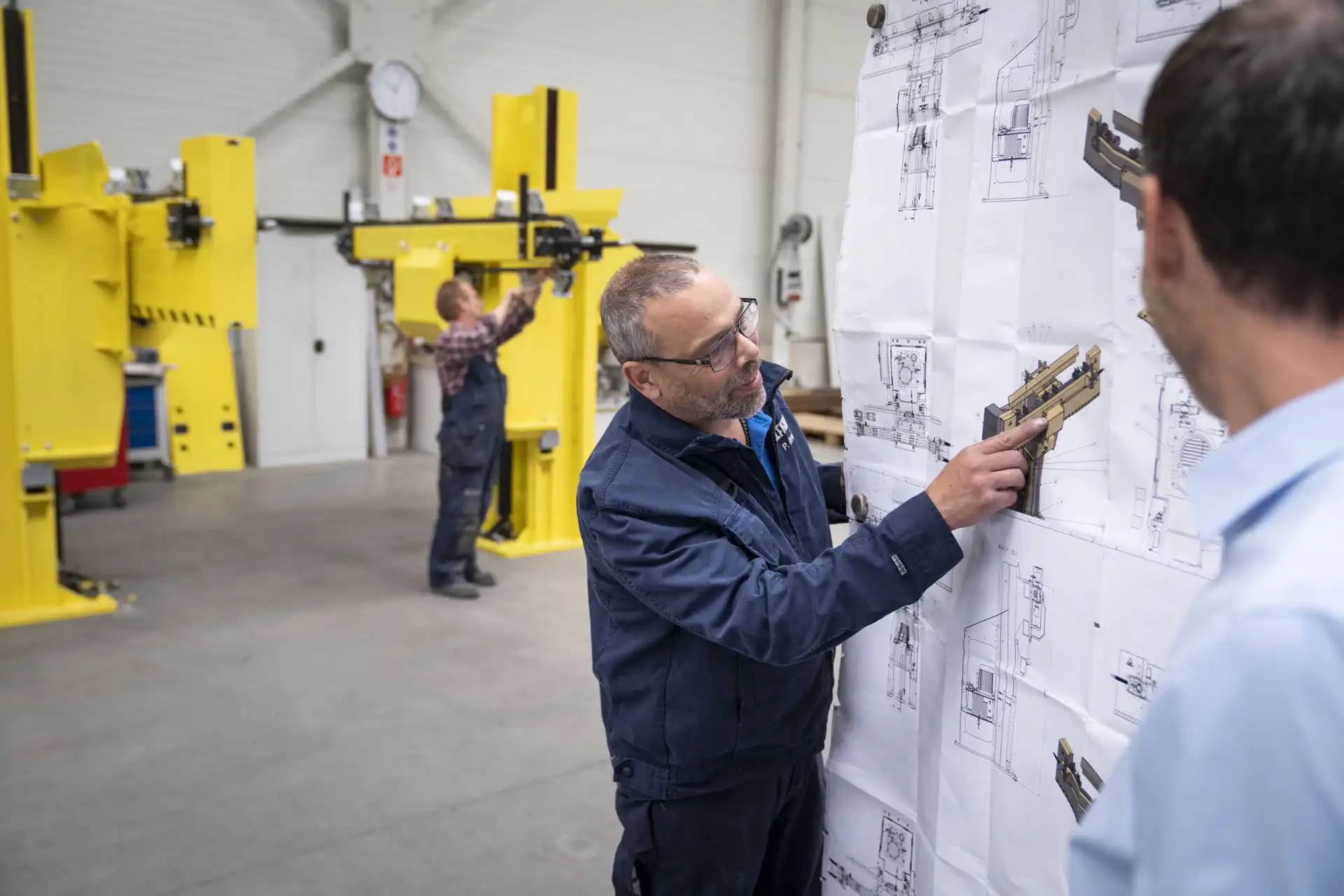 A man pointing at a technical drawing of a handling system for handling technology. Title: Handling technology for the efficient handling of heavy loads.